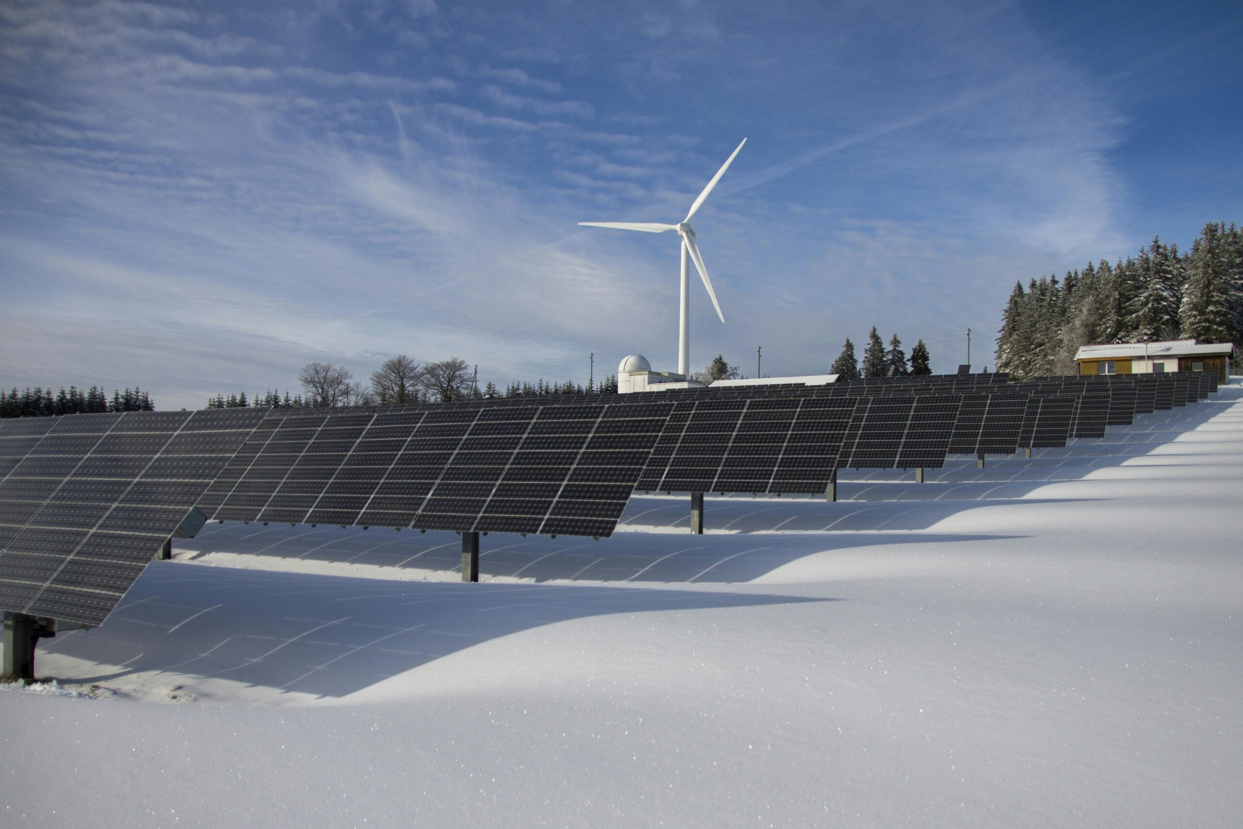 Solar panels and wind turbine in a snowy landscape, showcasing renewable energy sources.